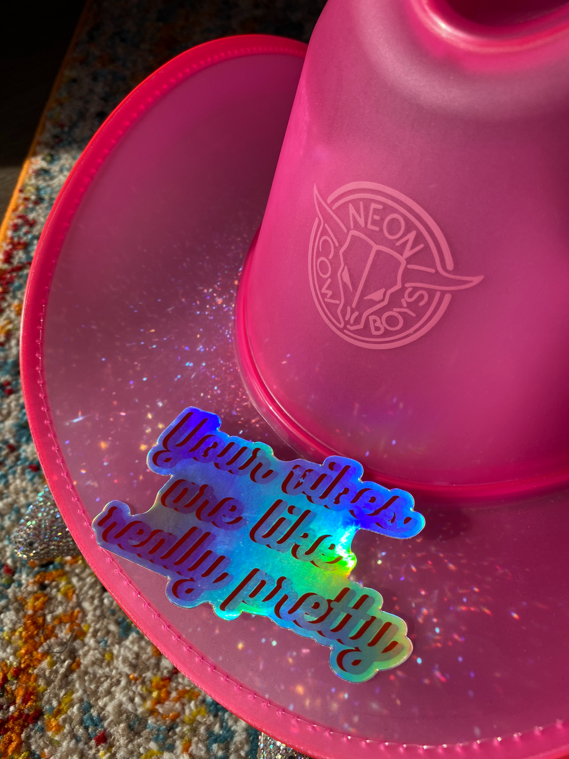 "Your vibes are really pretty" slogan holographic sticker displayed on a neon cowboy hat
